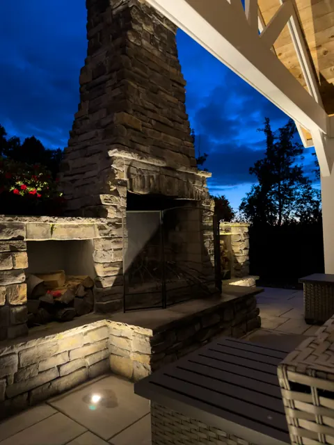 Stone outdoor fireplace with hardscape lighting under a pavilion