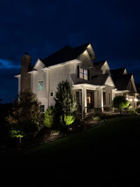 White two-story home with facade uplighting at dusk