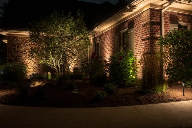 Brick home with lit ornamental tree and garden bed