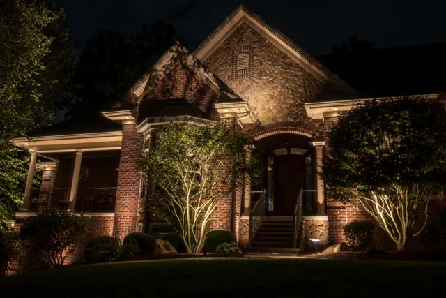 Brick home with lit entry, trees and front porch