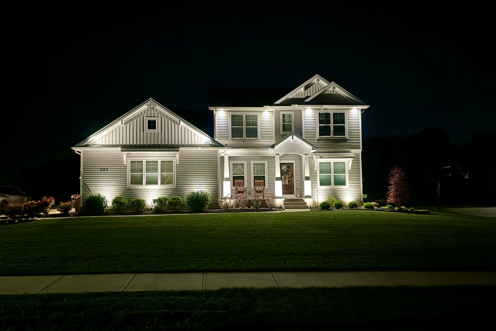Landscape lighting on a white farmhouse, uplights on the facade and beds