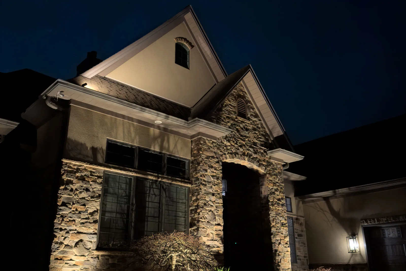 Stone and shingle home with architectural uplighting at dusk