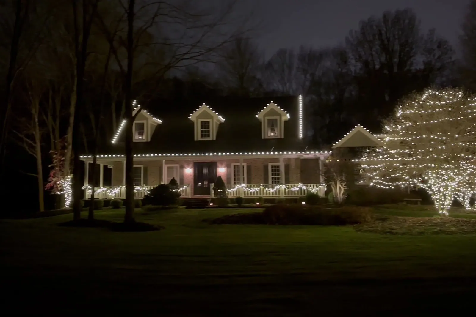Christmas roofline lights running the full length of a home with lit trees