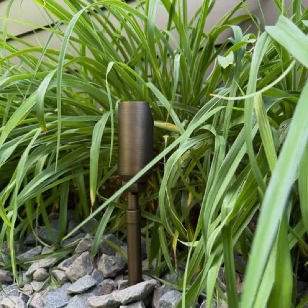 Metal spotlight fixture on a stake among tall ornamental grass and river rock