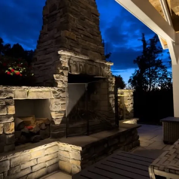 Outdoor stone fireplace and patio lit at dusk