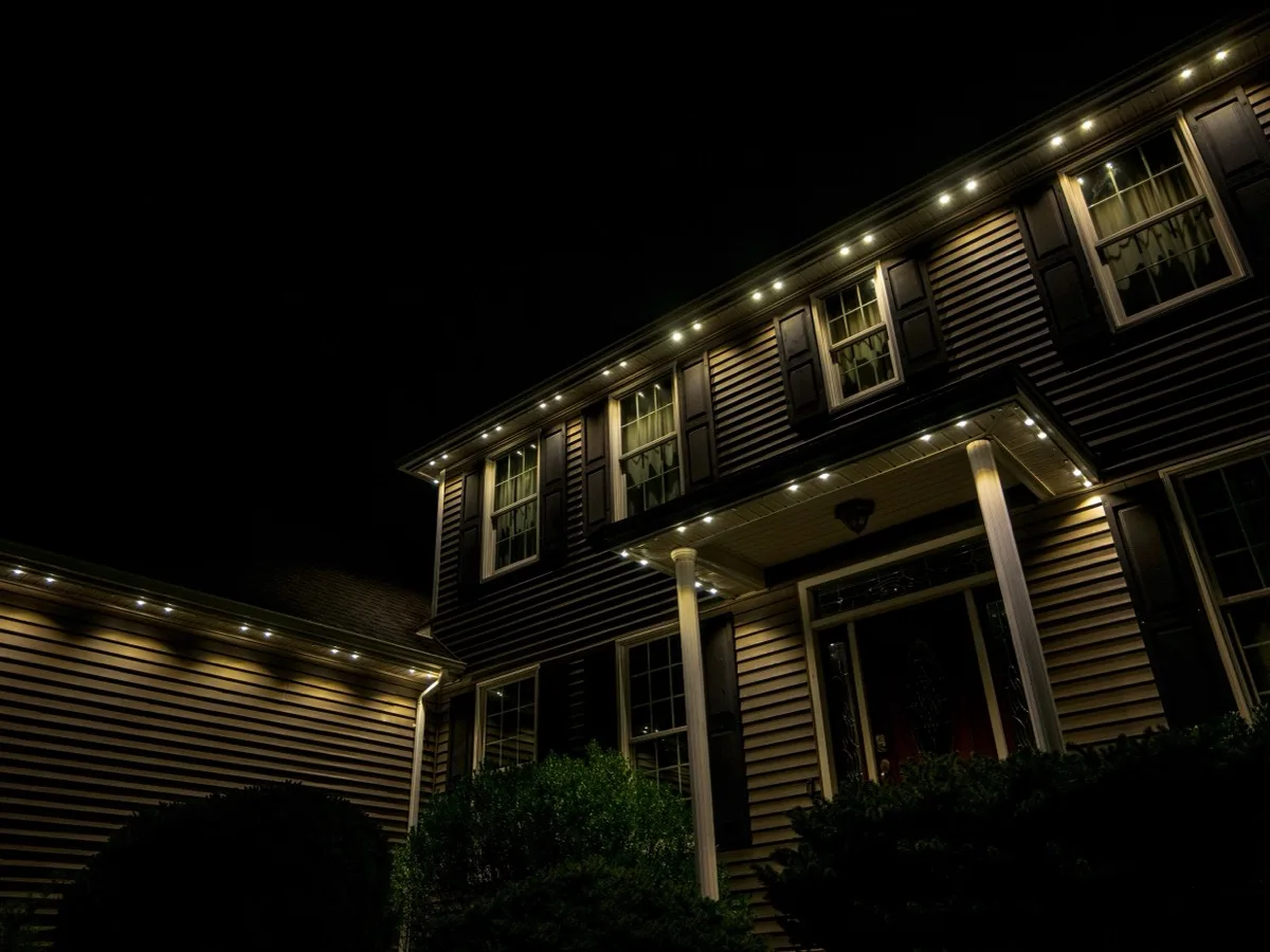 Warm white permanent lights along the roofline and porch of a two-storey home at night